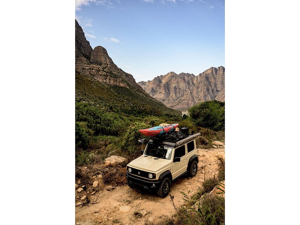 Suzuki Jimny avec une galerie Front Runner et un kayak orange dans un paysage de montagne