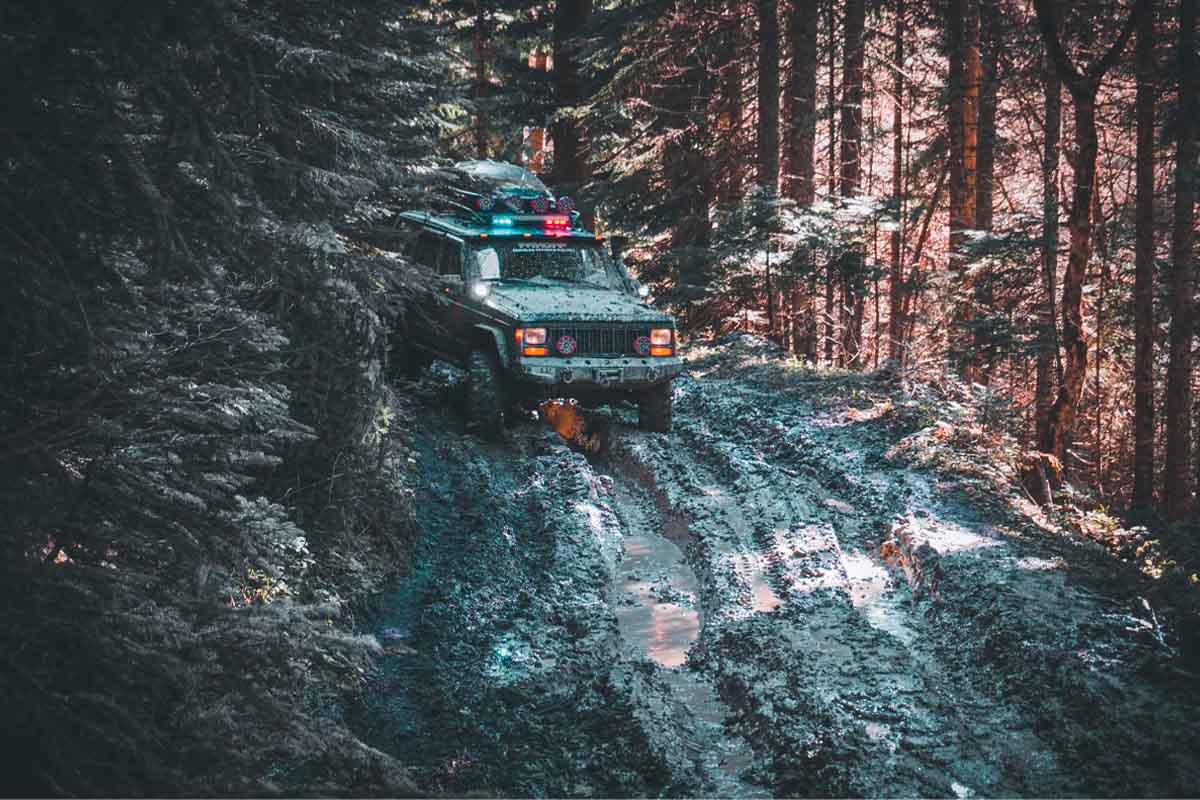 Une jeep préparée pour l'overlanding en train de passer dans de la boue épaisse, un terrain très difficile.